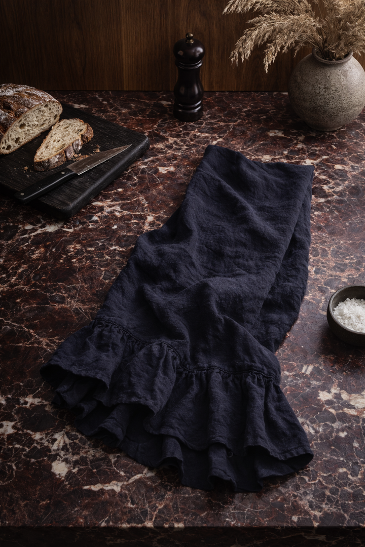 Black Lisiére Tea Towel on a dark marble surface with bread and a pepper grinder.
