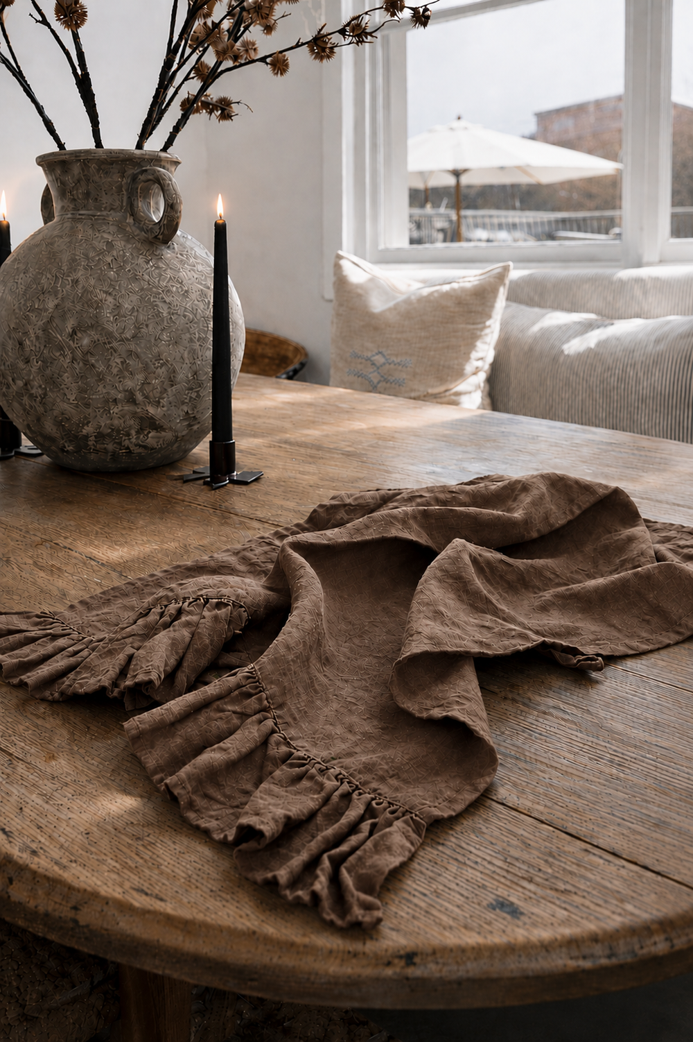 Saltbush Living chocolate coloured Lisiére Linen Tea Towel with a frill on a wooden dining table next to candles and a vase