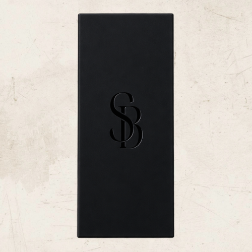 A tall, narrow black rectangular matchbox with Saltbush Living embossed stylised 'SB' monogram centered on the front, photographed against a light textured beige background.