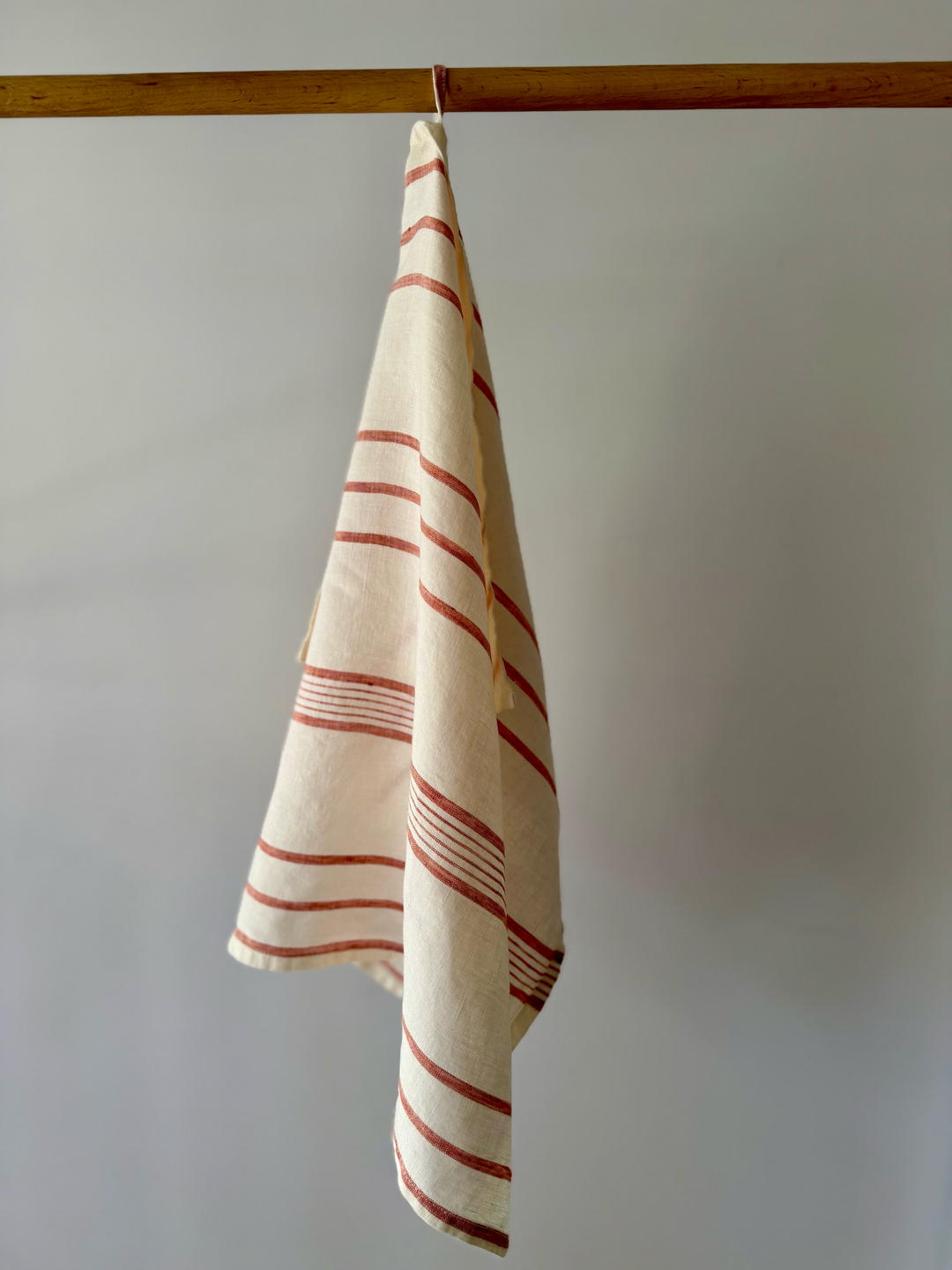 A red & white striped linen kitchen tea towel hanging from a wooden rod against a plain light grey wall.